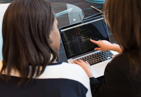 Two women working together on software programming indoors, focusing on code.