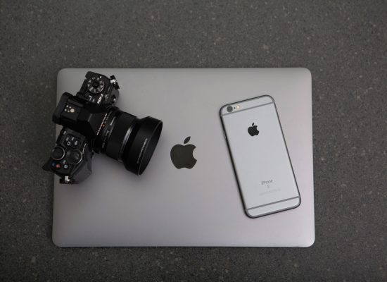 High-angle shot of DSLR camera, MacBook, and iPhone on textured surface, showcasing modern technology essentials.