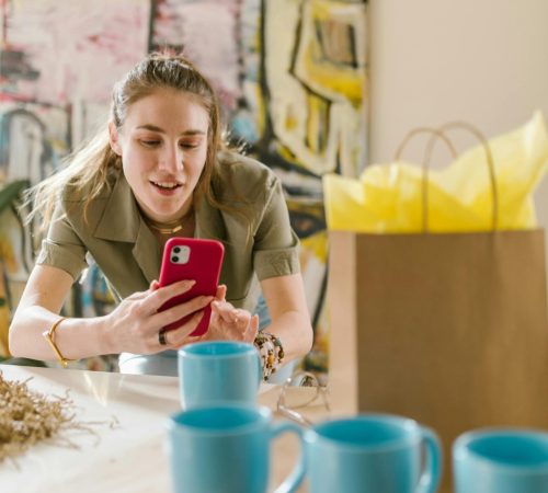 Woman using smartphone surrounded by cups and bag, ideal for online business themes.